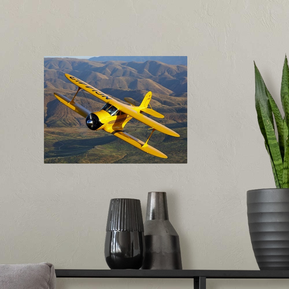 A modern room featuring Photograph of a Beechcraft D-17 Staggerwing single propeller biplane flying over rolling hills.