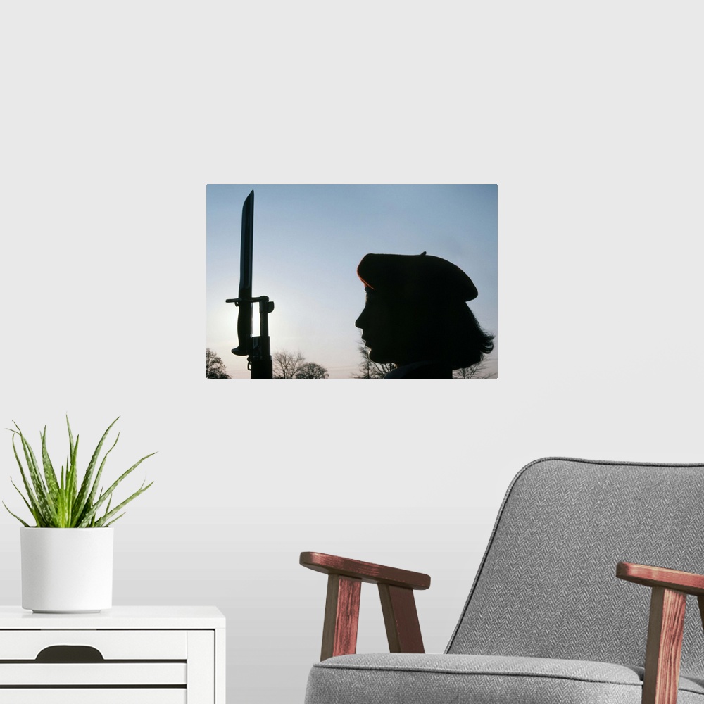 A modern room featuring A Navy Flying Rifles Drill Team member stands at attention holding the M1 Garrand rifle