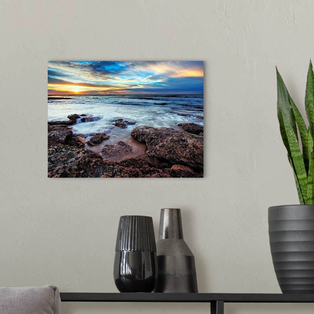 A modern room featuring Photograph taken of the ocean that rushes up onto rocks that are pictured in the foreground. The ...