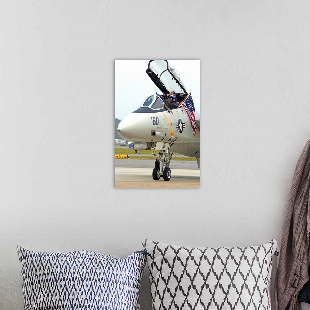 A bohemian room featuring Air crewmen wave from their F14D Tomcat as they taxi