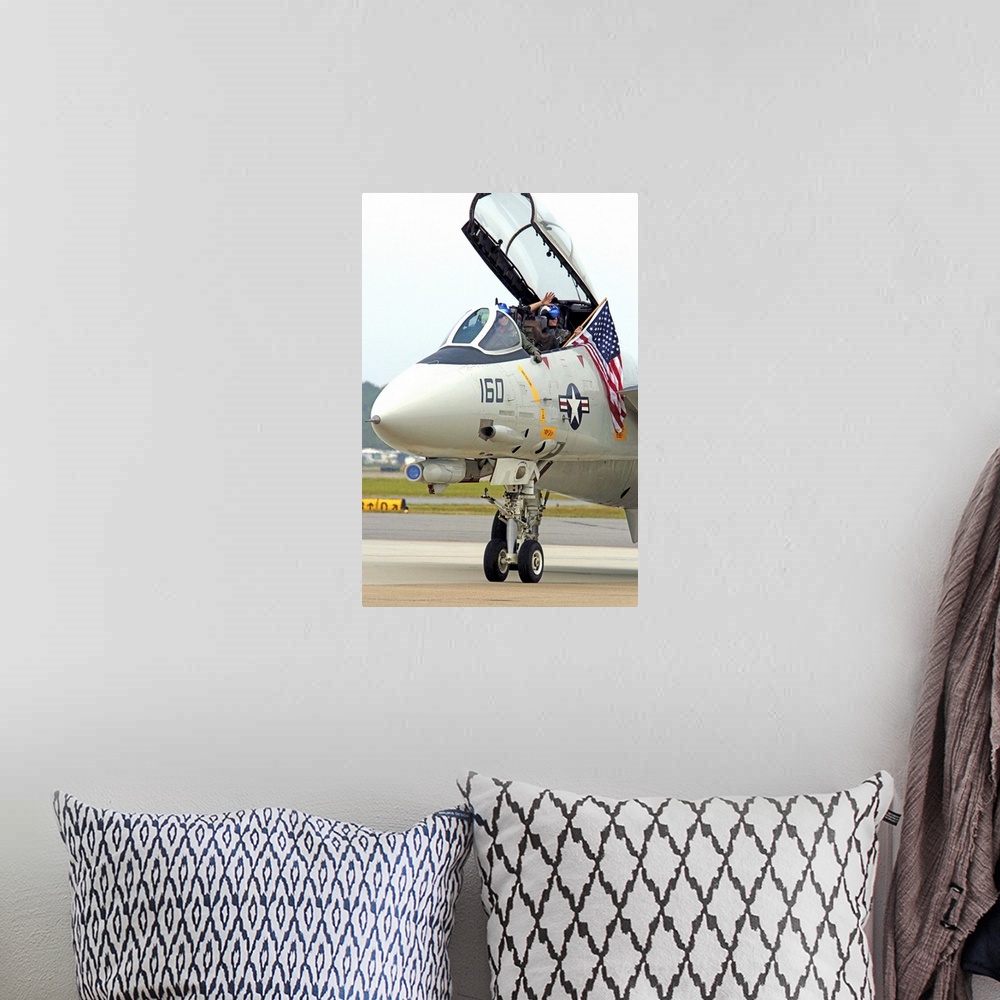 A bohemian room featuring Air crewmen wave from their F14D Tomcat as they taxi