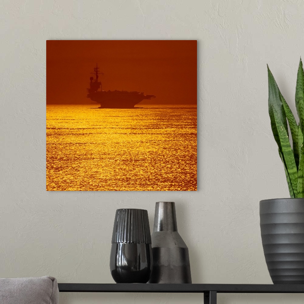 A modern room featuring Square photograph on a large wall hanging of a silhouetted aircraft carrier on vivid golden water...