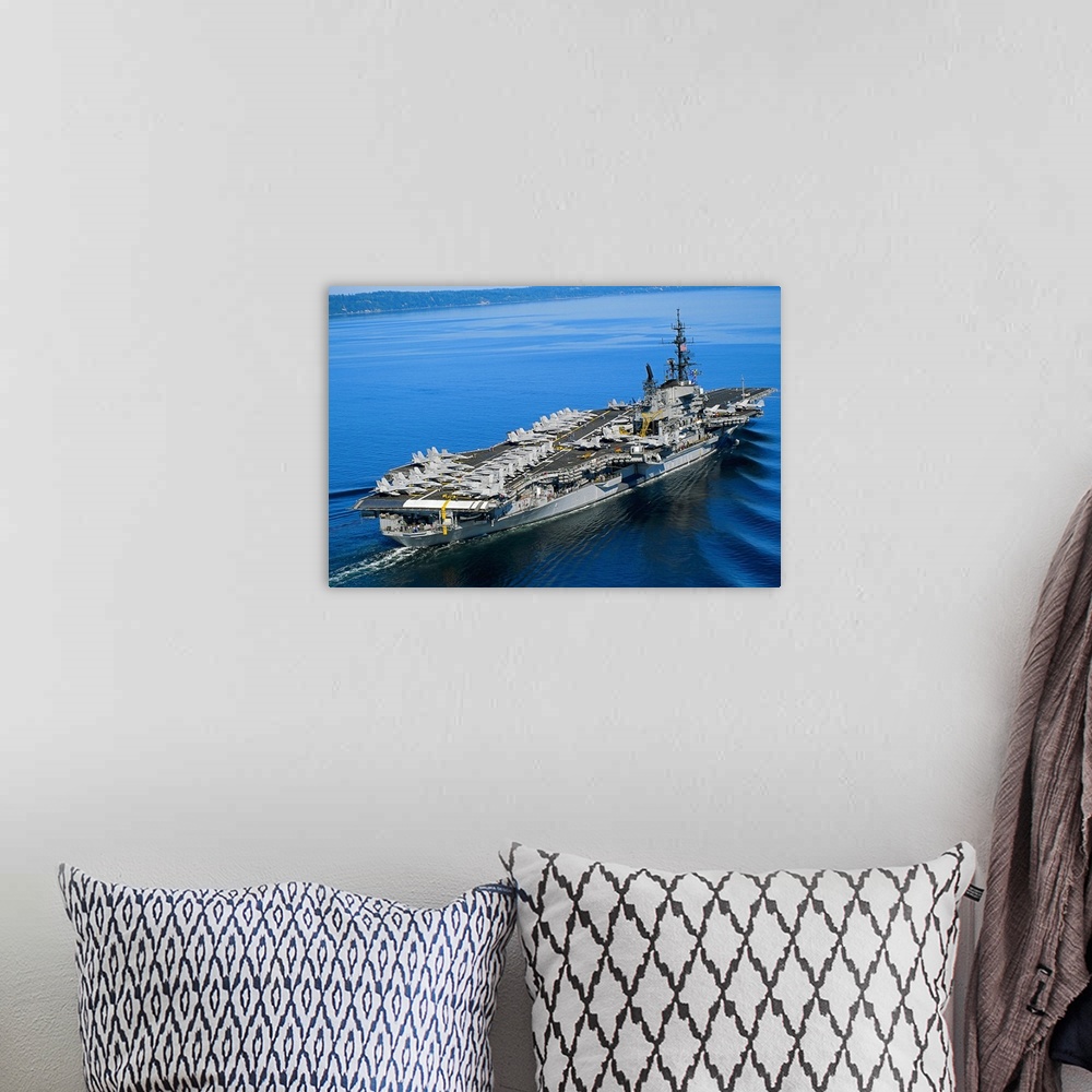 A bohemian room featuring An aerial photograph of a naval warship not far off the coast its deck covered with fighter jets.