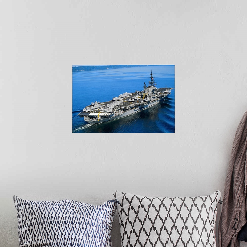 A bohemian room featuring An aerial photograph of a naval warship not far off the coast its deck covered with fighter jets.