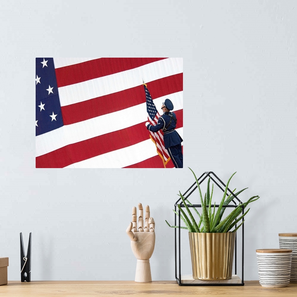 A bohemian room featuring A soldier stands in front of a massive American flag while holding a smaller flag during the chan...