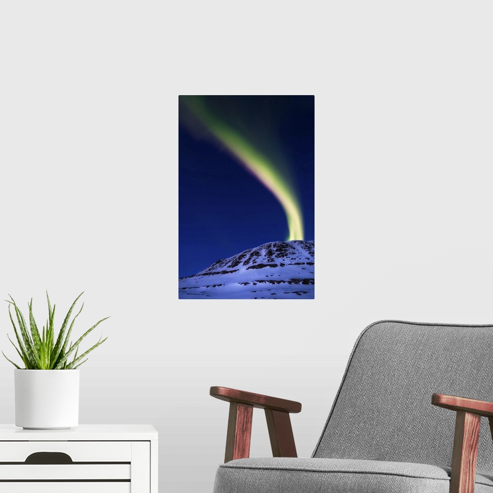 A modern room featuring A magnificent display of aurora borealis shooting up from Toviktinden Mountain in Troms County, N...
