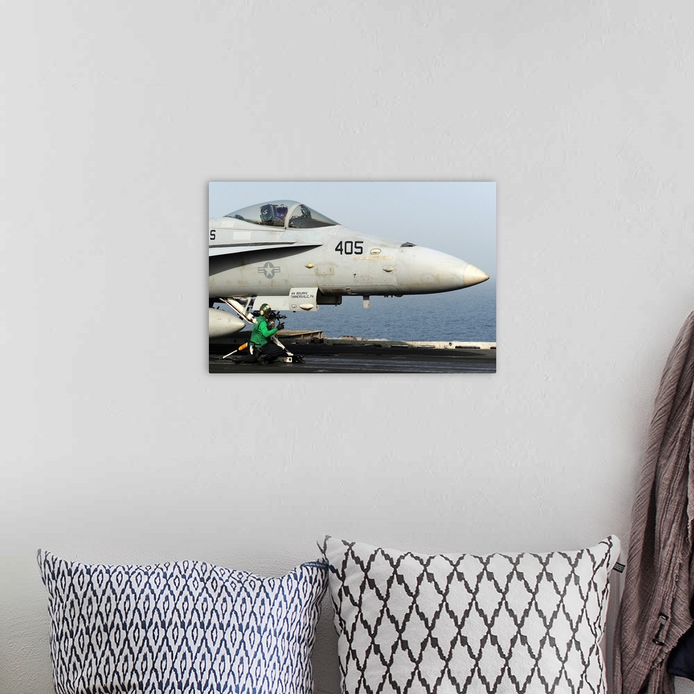 A bohemian room featuring An aviation boatswain's mate guides an F/A-18C Hornet into a catapult.