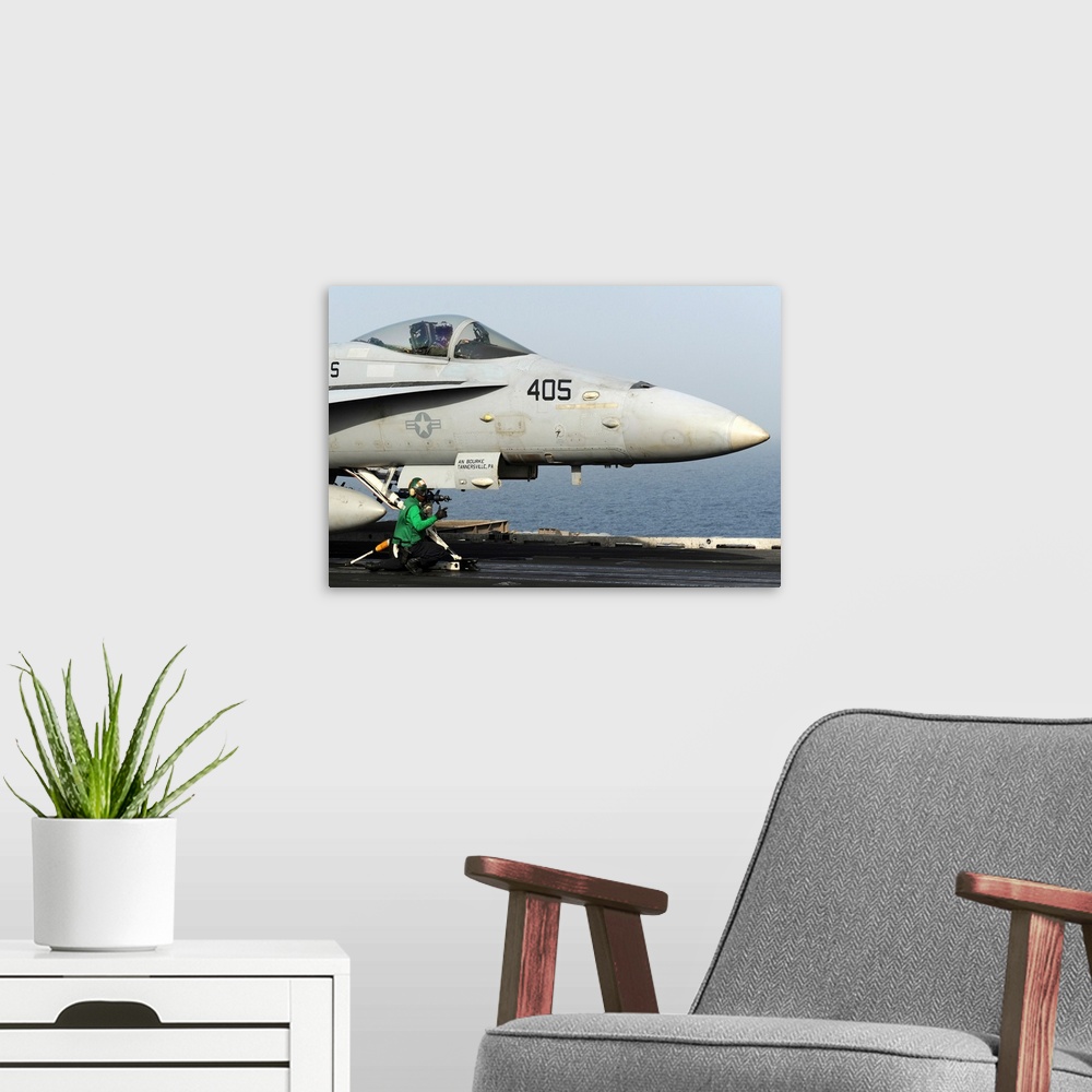 A modern room featuring An aviation boatswain's mate guides an F/A-18C Hornet into a catapult.