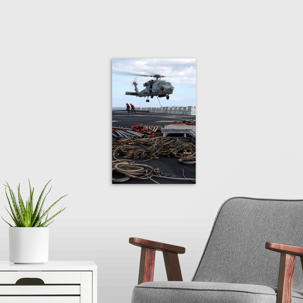 A modern room featuring An HH-60H Seahawk helicopter prepares to lift a crate of ordnance.