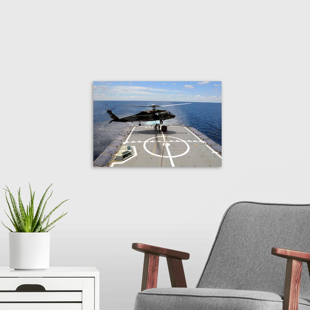 A modern room featuring An SH-60F Sea Hawk helicopter lowers pallets onto HMAS Ballarat.