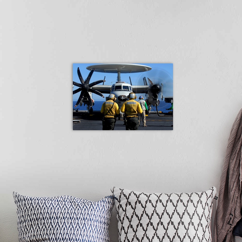 A bohemian room featuring Flight deck directors watch as pilots of an E2C Hawkeye startup their engines