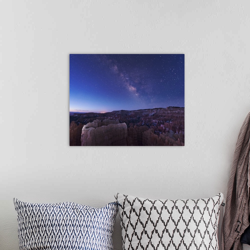 A bohemian room featuring The rising sun begins fading away the nightime Milky Way over the needle rock formations of Bryce...