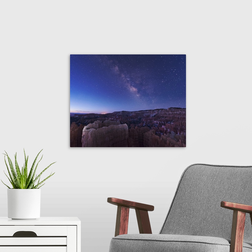 A modern room featuring The rising sun begins fading away the nightime Milky Way over the needle rock formations of Bryce...