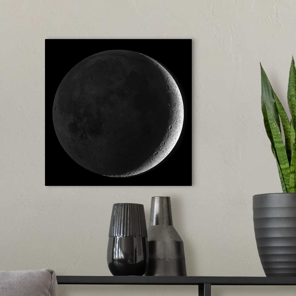 A modern room featuring Giant square wall picture of the moon, dark except a small sliver on one side, surrounded by a bl...