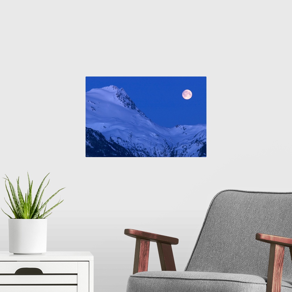 A modern room featuring Large image on canvas of a full moon to the right of a tall snowy mountain ridge.
