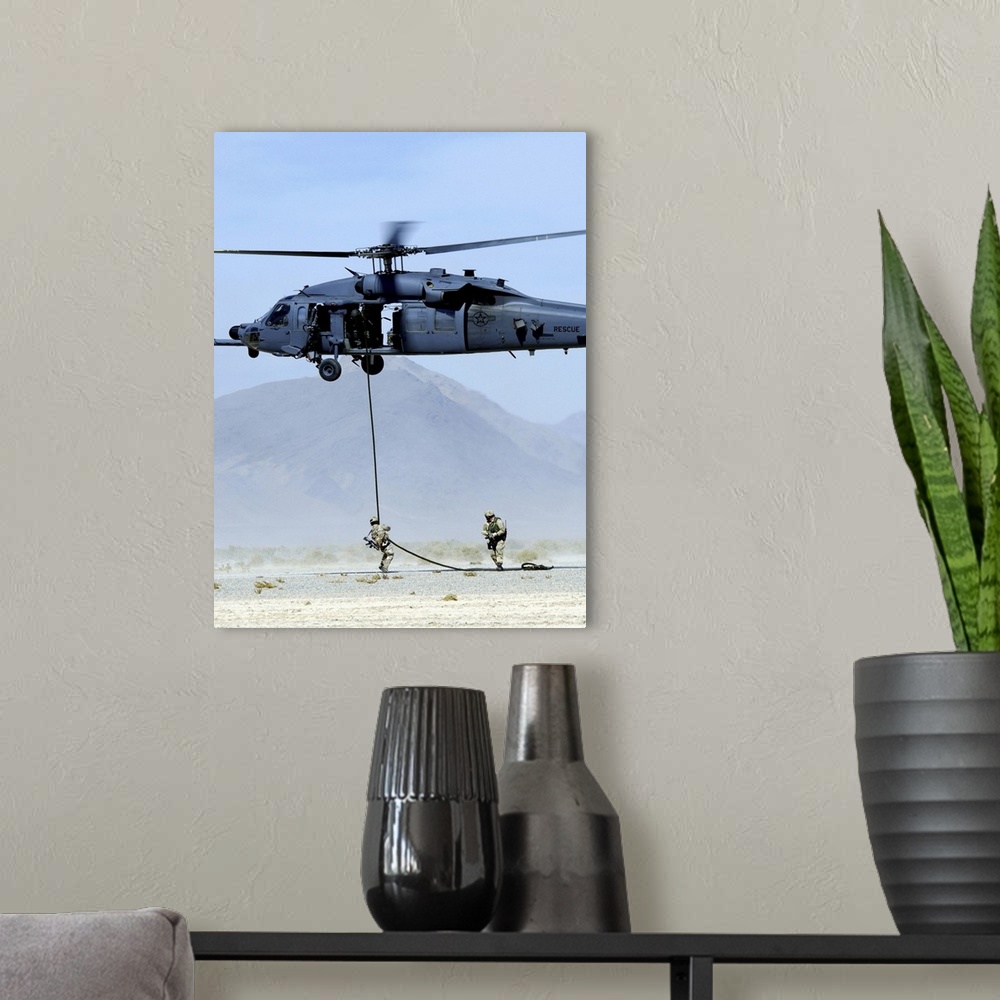 A modern room featuring Pararescuemen descend from an HH-60 Pave Hawk helicopter.