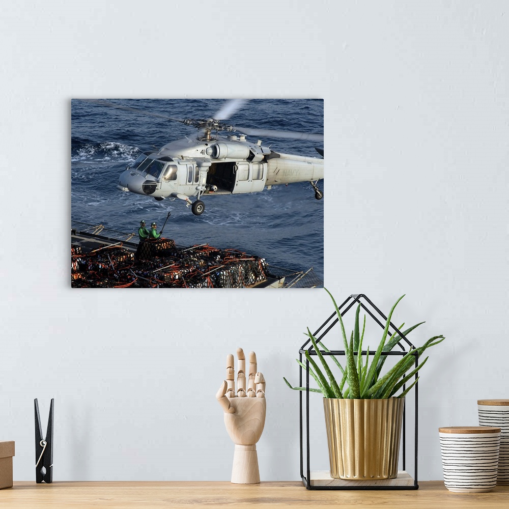 A bohemian room featuring Sailors attach pallets of supplies to an MH-60S Knighthawk.