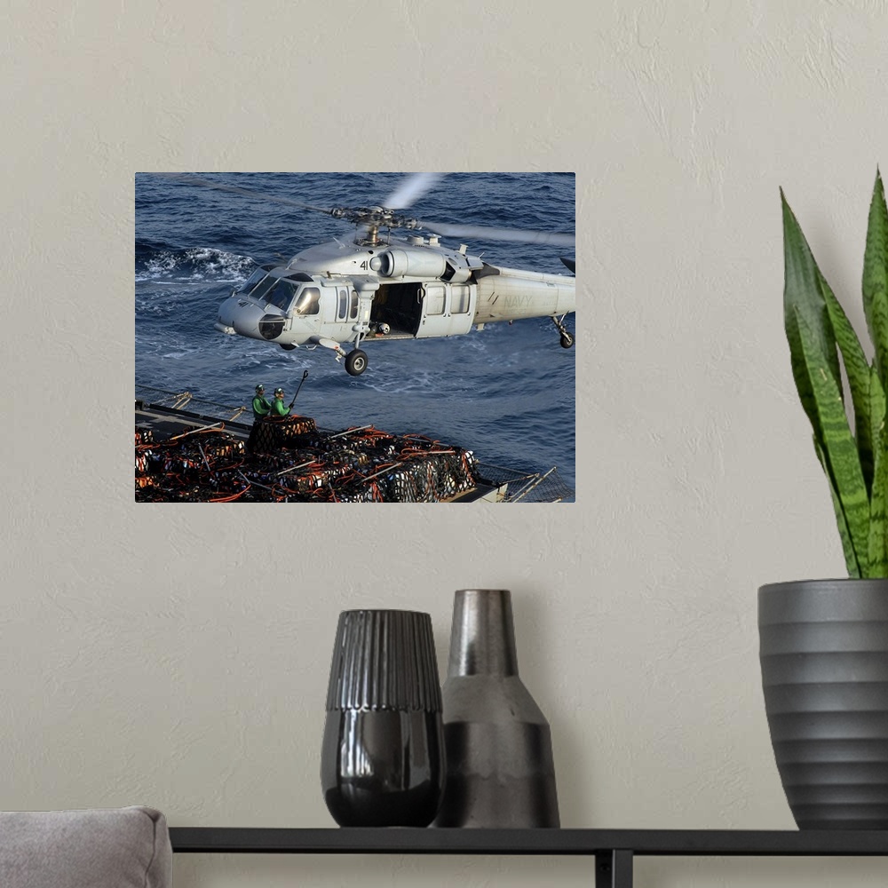 A modern room featuring Sailors attach pallets of supplies to an MH-60S Knighthawk.