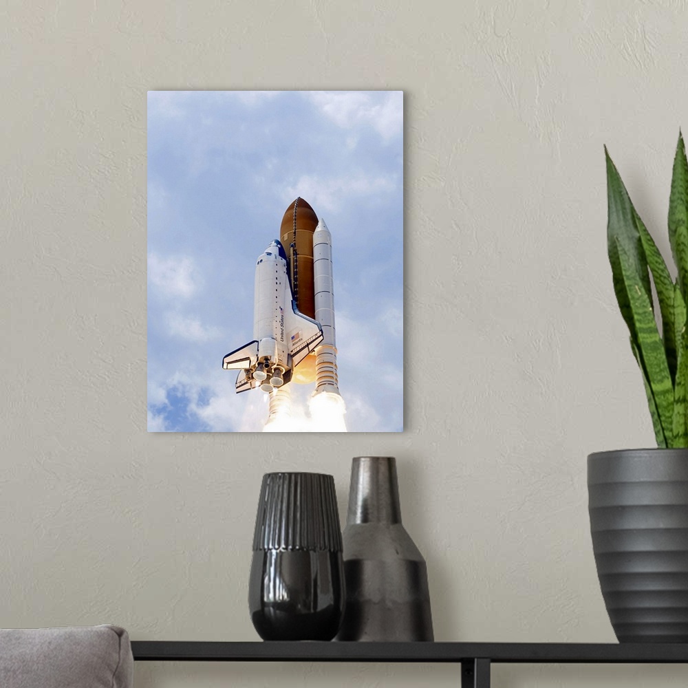 A modern room featuring Space Shuttle Atlantis lifts off from its launch pad toward Earth orbit