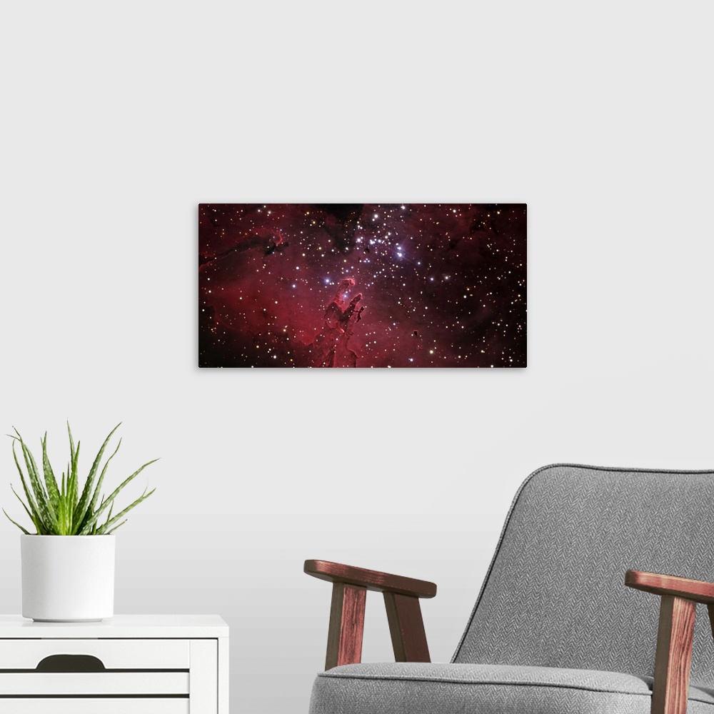 A modern room featuring An oversized piece of the eagle nebula that has bright stars scattered across the print with a re...