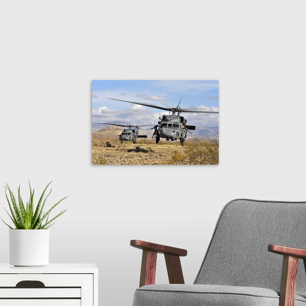A modern room featuring A couple of military copters hovering a few feet off the ground in a desert during a training exe...