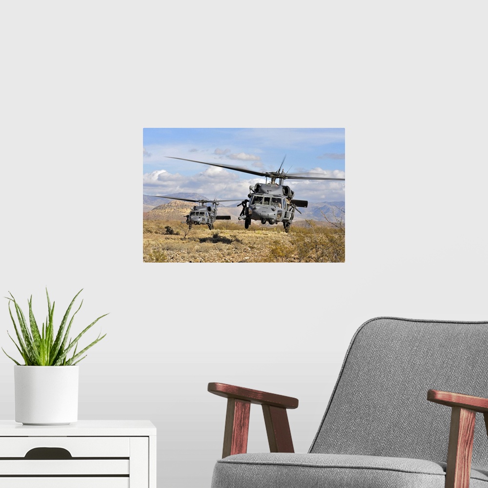 A modern room featuring A couple of military copters hovering a few feet off the ground in a desert during a training exe...
