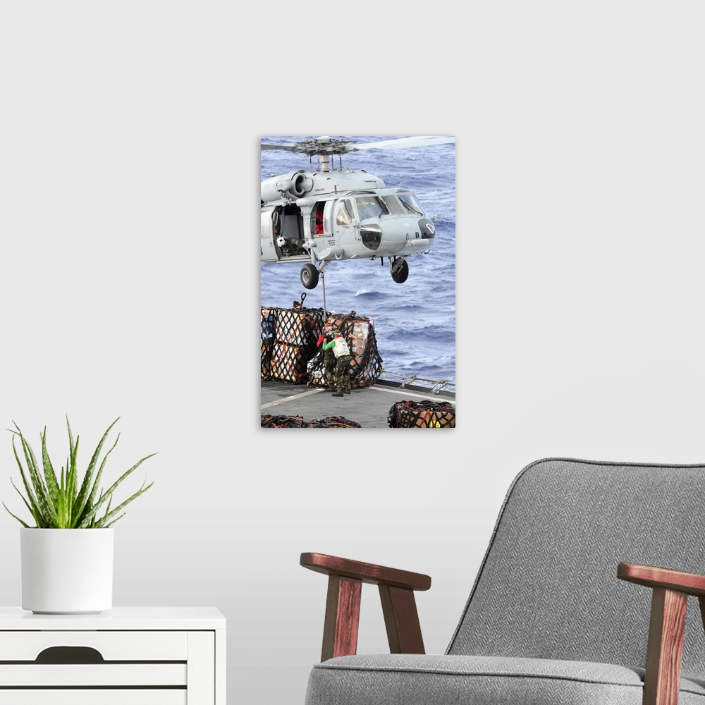 A modern room featuring U.S. Sailors connect a cargo pendant to an MH-60S Seahawk helicopter.