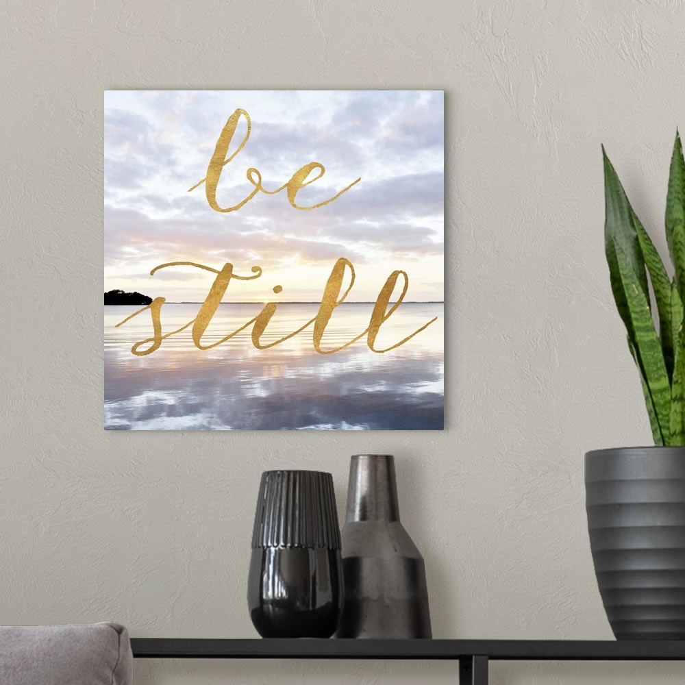 A modern room featuring "Be Still" hand written in gold letters over an image of the sea at dawn.