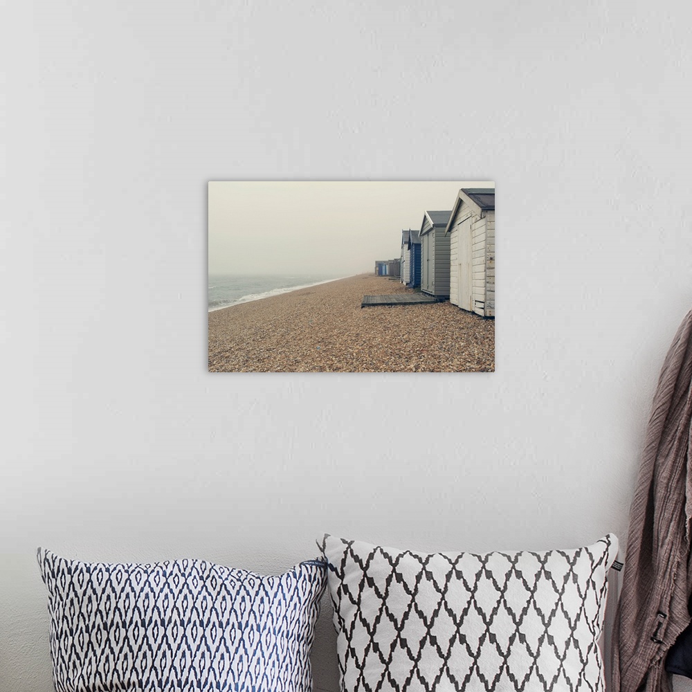 A bohemian room featuring A photograph of a pebbled beach with a row of beach huts on an overcast day.