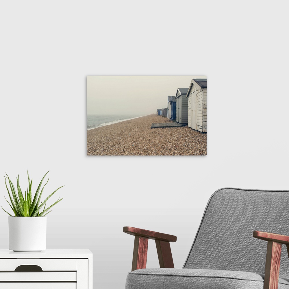 A modern room featuring A photograph of a pebbled beach with a row of beach huts on an overcast day.