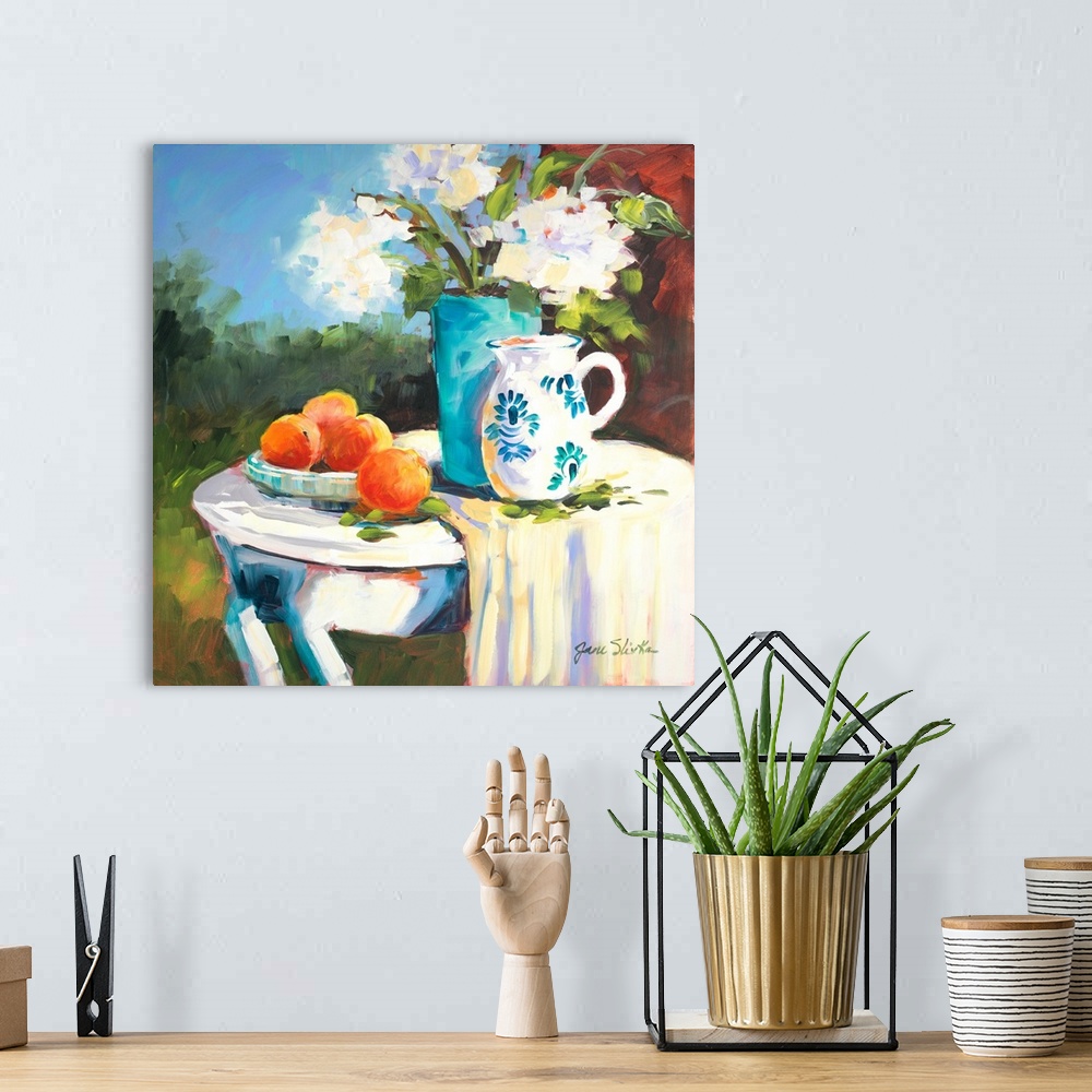 A bohemian room featuring Painting of a table with a plate of oranges, a blue vase, and a pitcher.