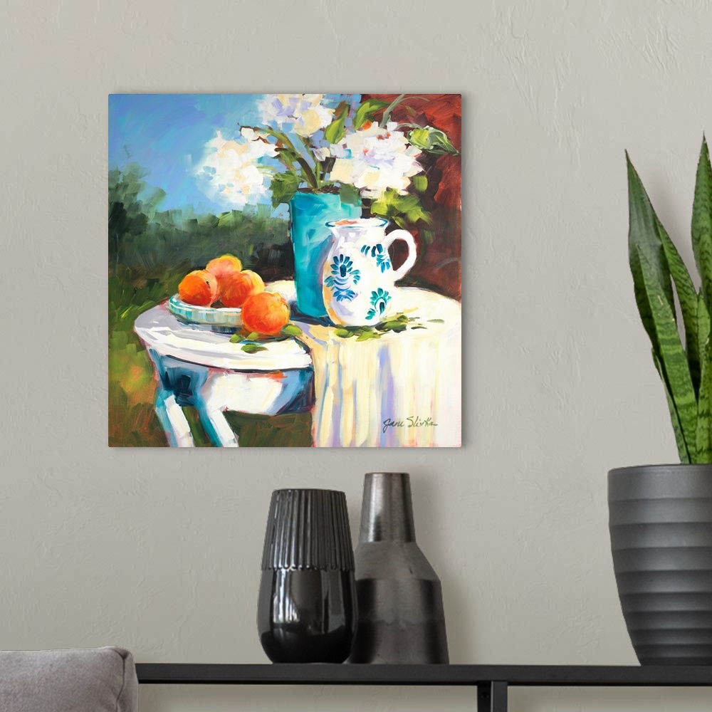 A modern room featuring Painting of a table with a plate of oranges, a blue vase, and a pitcher.