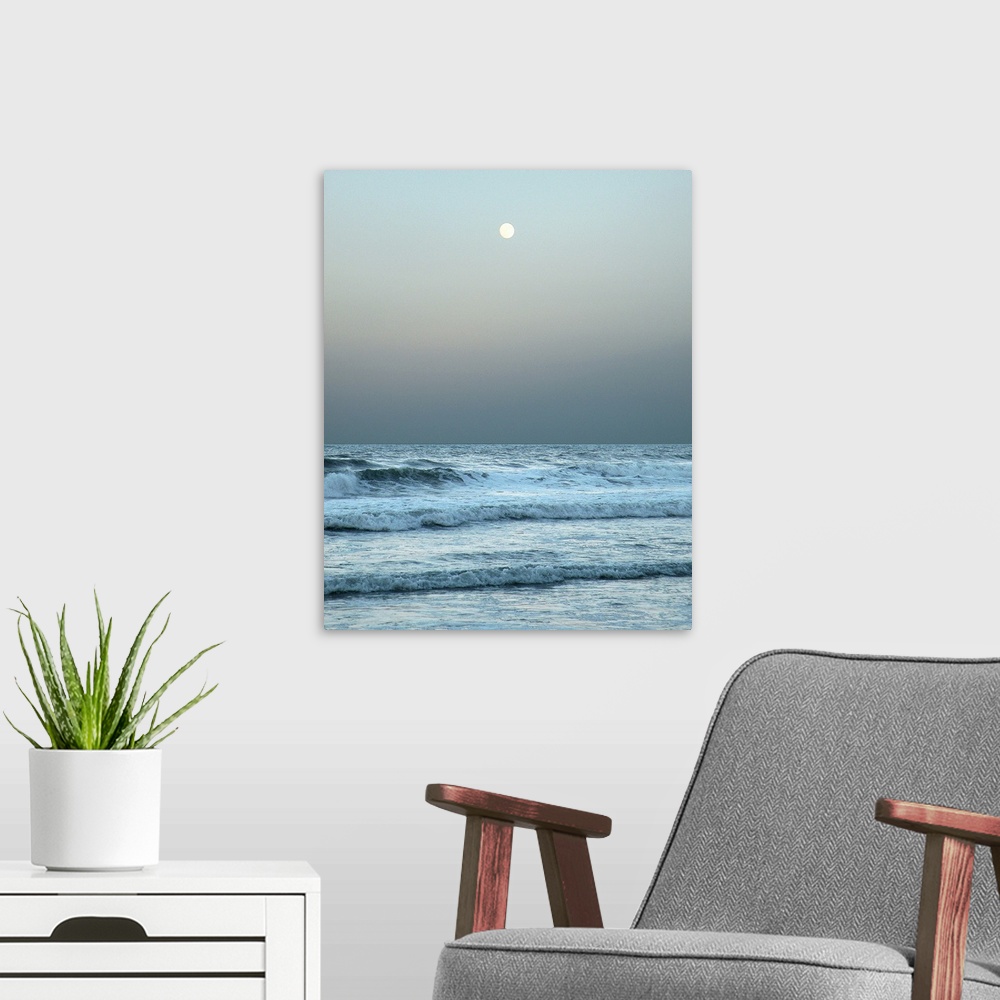 A modern room featuring A gray toned photograph of the ocean with a full moon.