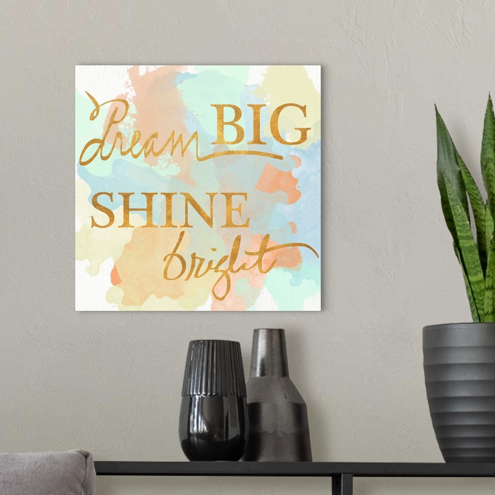 A modern room featuring "Dream Big Shine Bright" written in a shiny gold font on a pastel colored watercolor background.