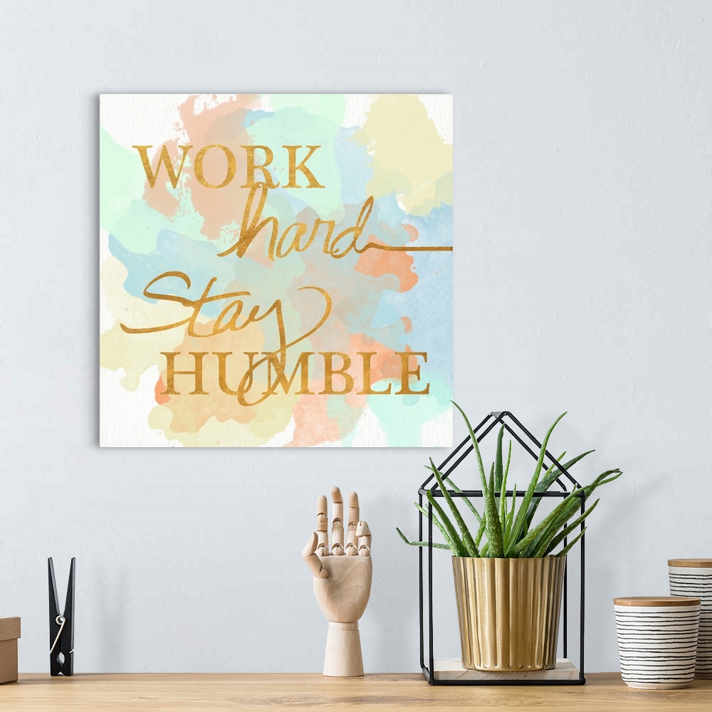 A bohemian room featuring "Work Hard Stay Humble"  written in a shiny gold font on a pastel colored watercolor background.