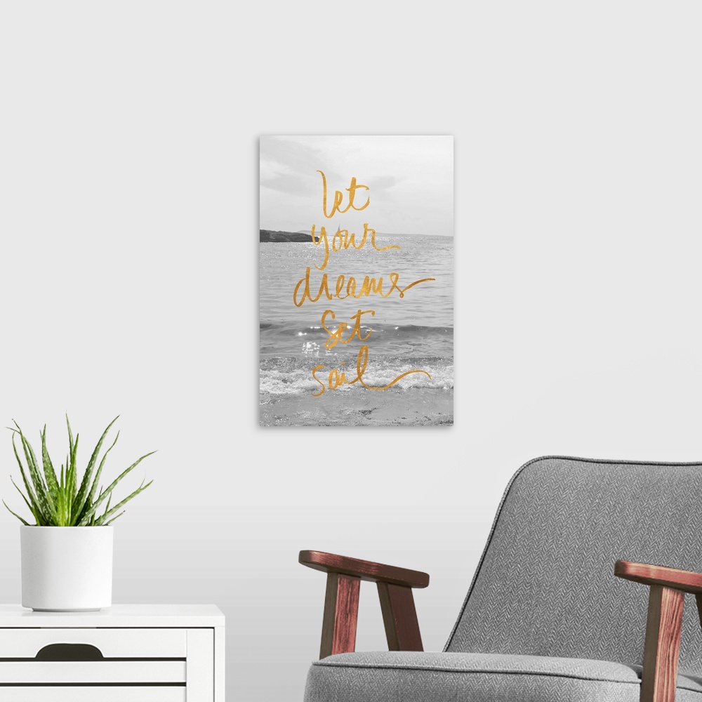A modern room featuring "Let Your Dreams Set Sail" written in gold on top of a black and white photograph of the ocean wi...