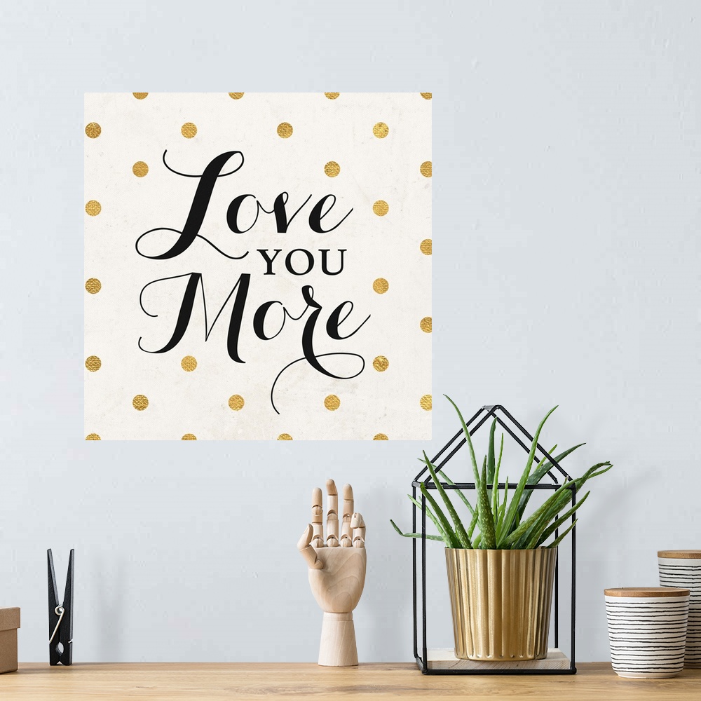 A bohemian room featuring The words "Love You More" in black script on a cream background with gold dots.