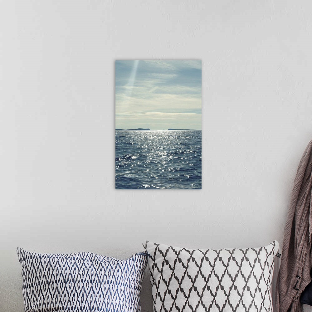 A bohemian room featuring A beautiful blue and gray toned photograph of the ocean water with the sun shining down on it.