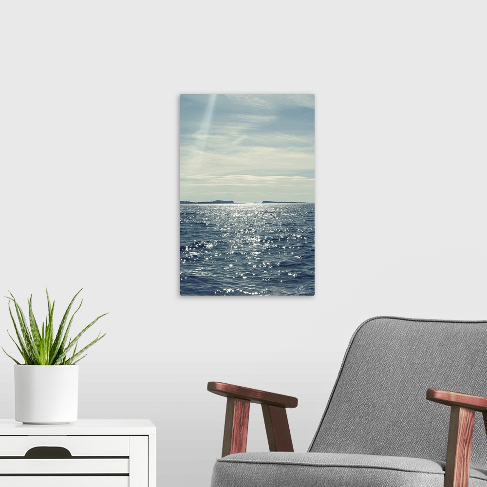 A modern room featuring A beautiful blue and gray toned photograph of the ocean water with the sun shining down on it.