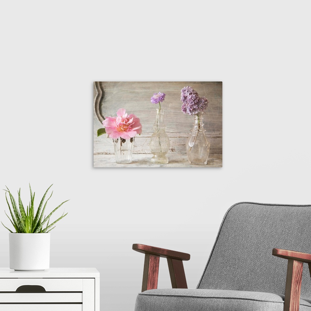 A modern room featuring Photograph of different flowers in a small glass vases, against a vintage wall.