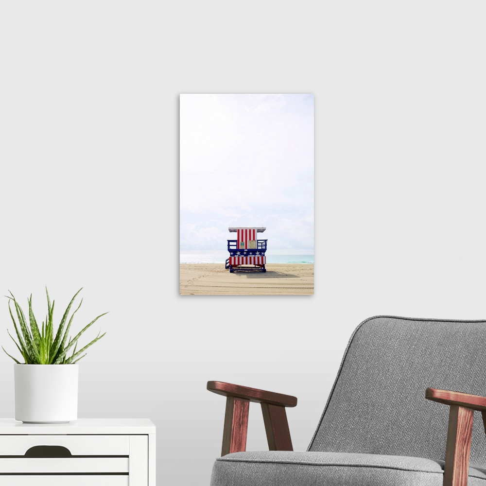 A modern room featuring Vertical photograph of an America themed lifeguard stand on an empty beach with calm waters and a...