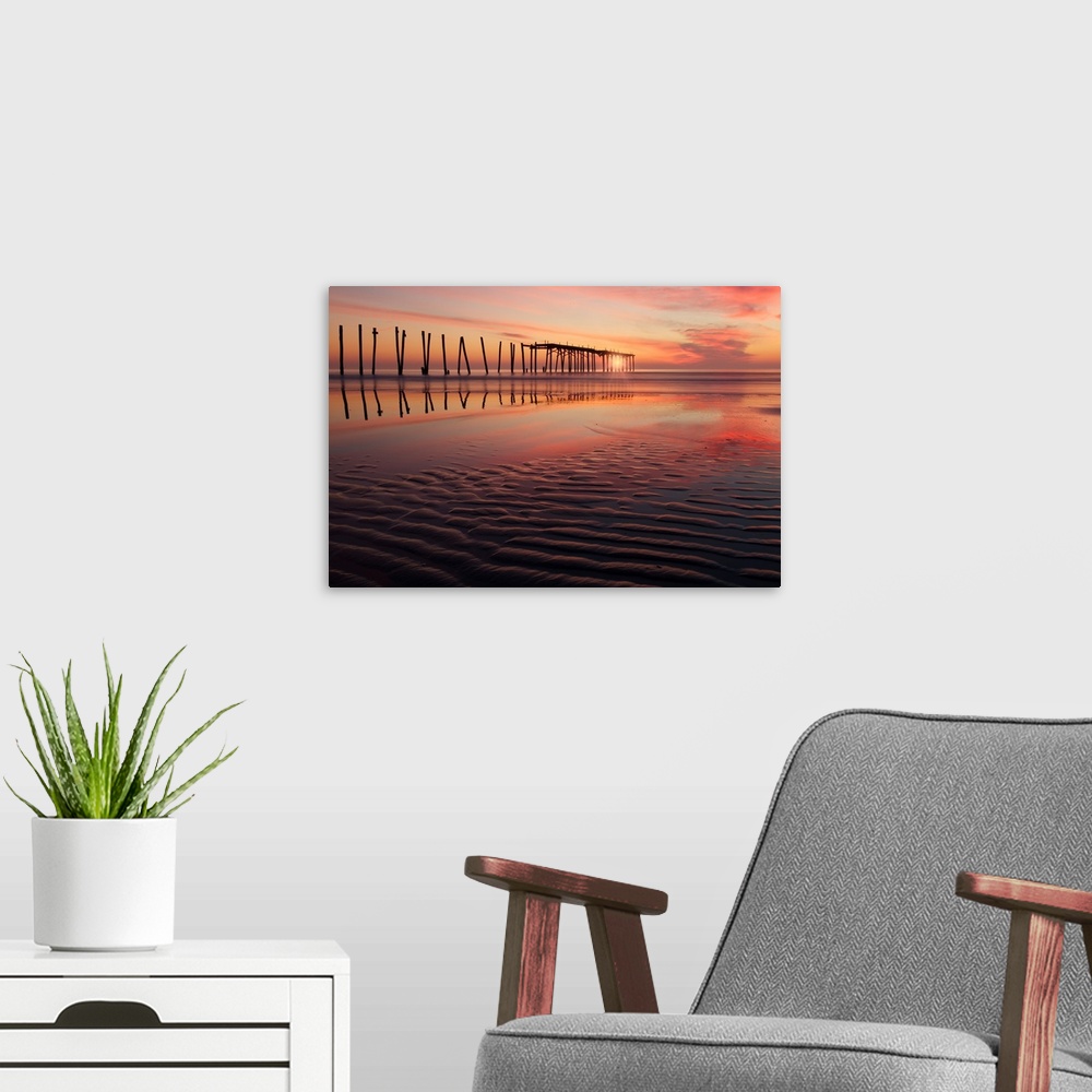 A modern room featuring Old wooden pier seen from the beach during a dramatic sunset.