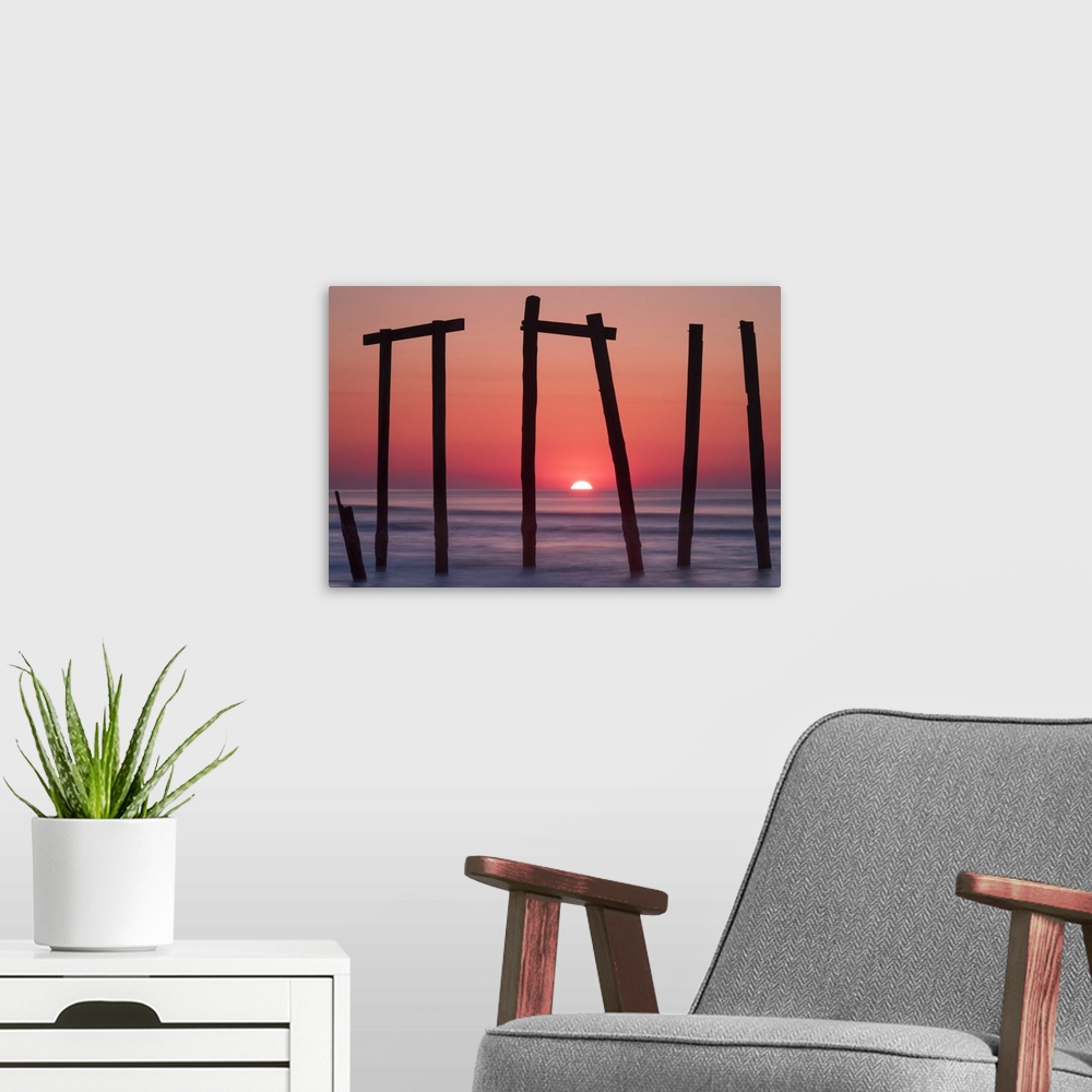 A modern room featuring Old pilings from a fishing pier framing a sunrise on the ocean horizon, Ocean City, New Jersey.
