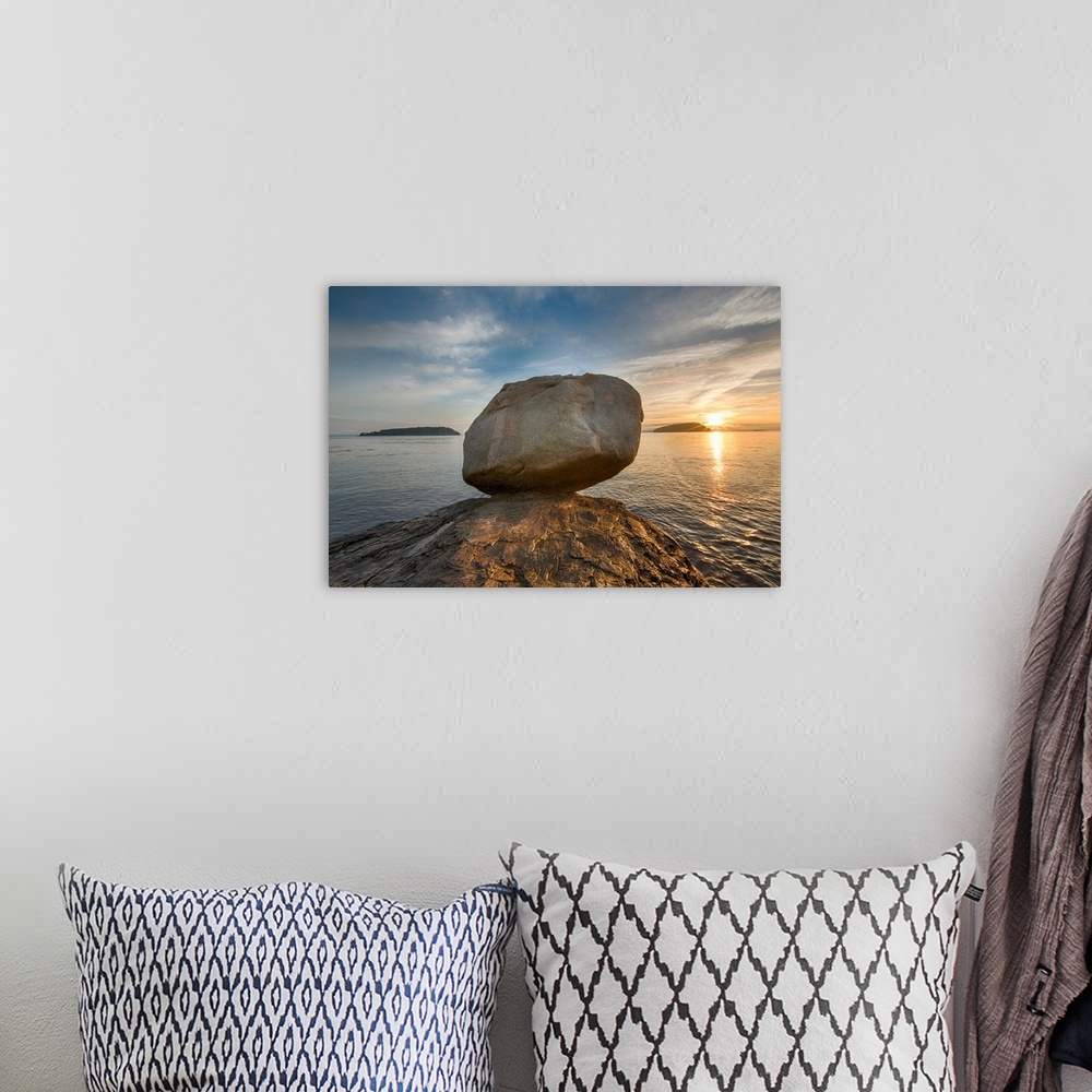 A bohemian room featuring A large rock on the beach in Acadia National Park in Maine, with the sun rising in the distance.