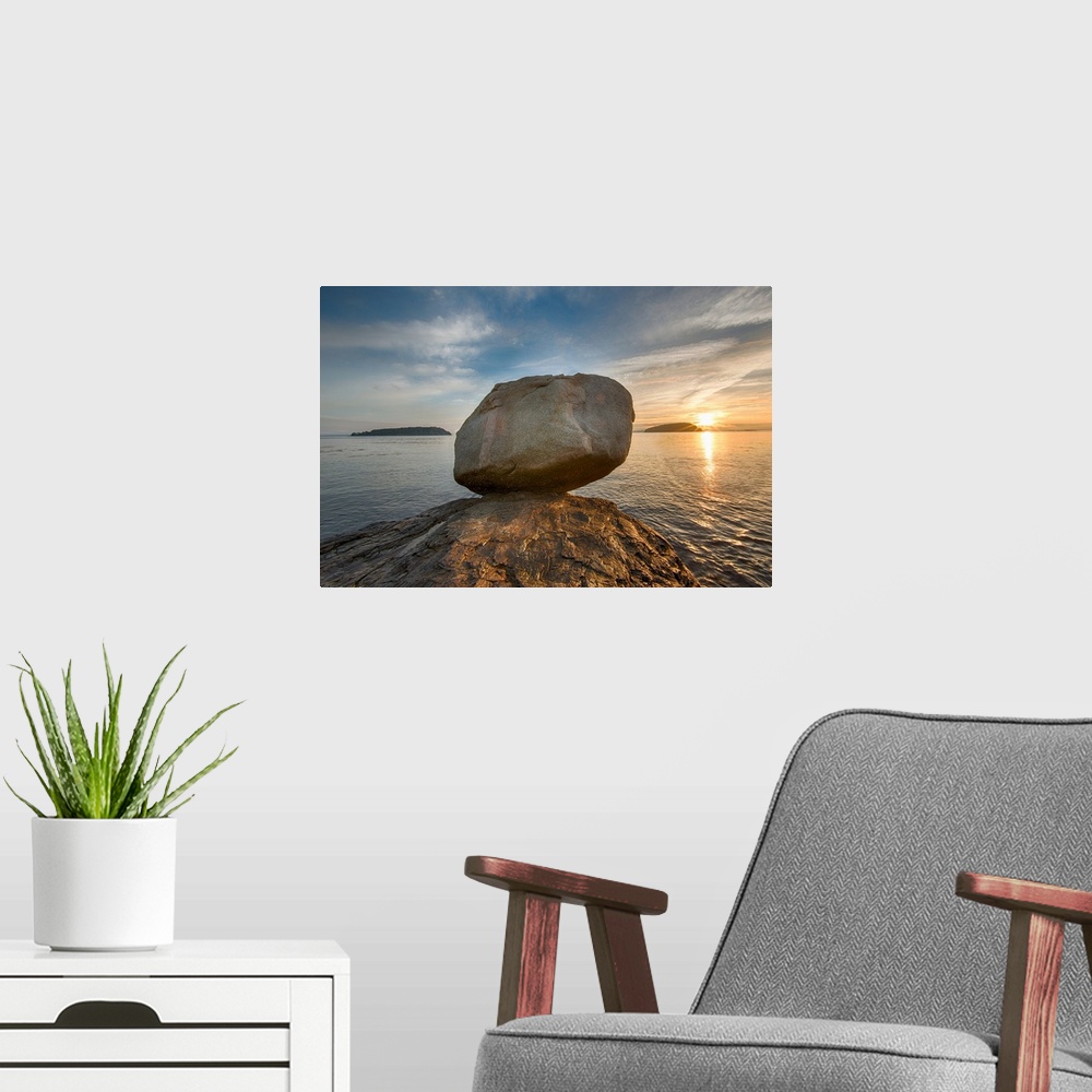 A modern room featuring A large rock on the beach in Acadia National Park in Maine, with the sun rising in the distance.