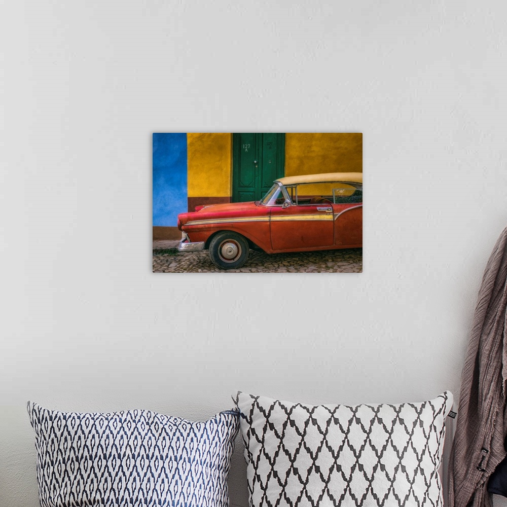 A bohemian room featuring A bright red vintage car parked against a yellow and blue wall with a green door in the streets o...