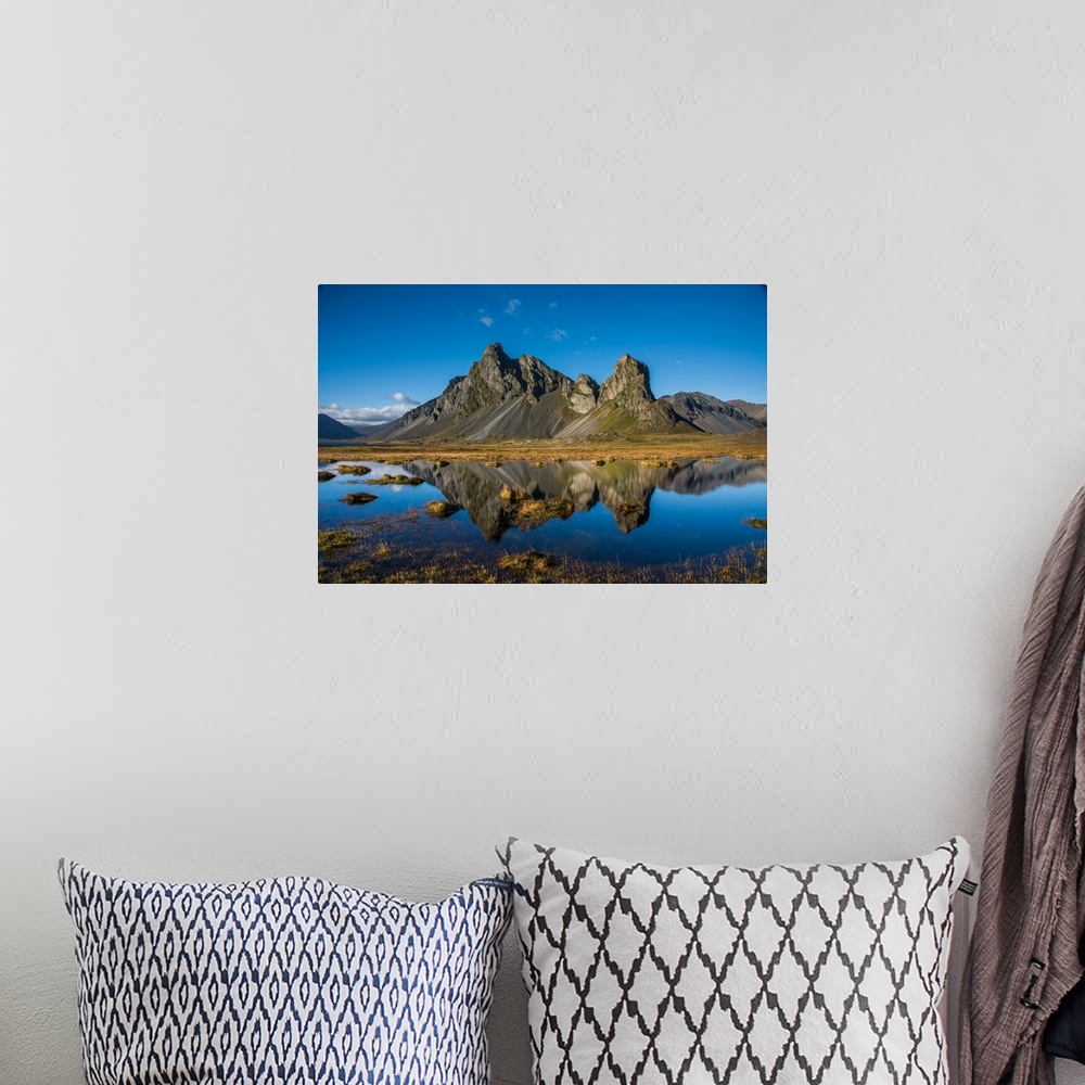 A bohemian room featuring Rugged mountains in Iceland, reflected in the clear lake below.