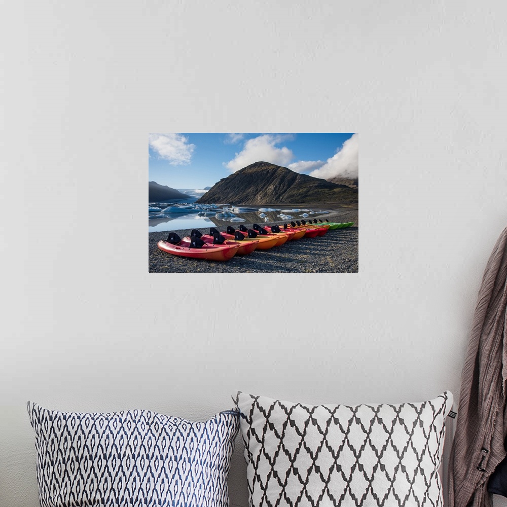 A bohemian room featuring A row of kayaks lined on the shore by an icy lake in Iceland.