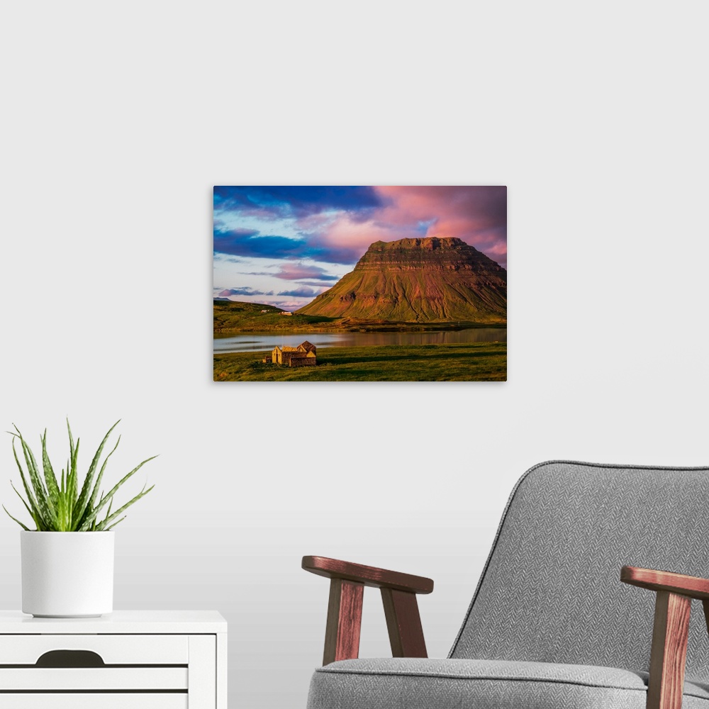 A modern room featuring A small house near a mountain with pink clouds at sunset in Iceland.