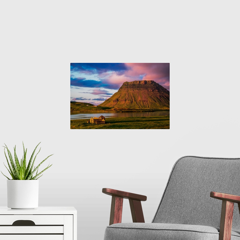 A modern room featuring A small house near a mountain with pink clouds at sunset in Iceland.
